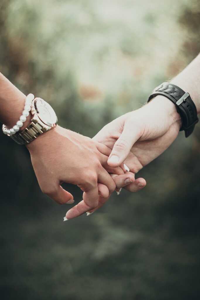 A heartfelt close-up of an interracial couple tenderly holding hands in an outdoor setting.