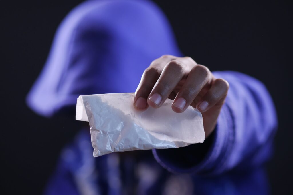Close-up of a hand holding a white sachet against a dark background.