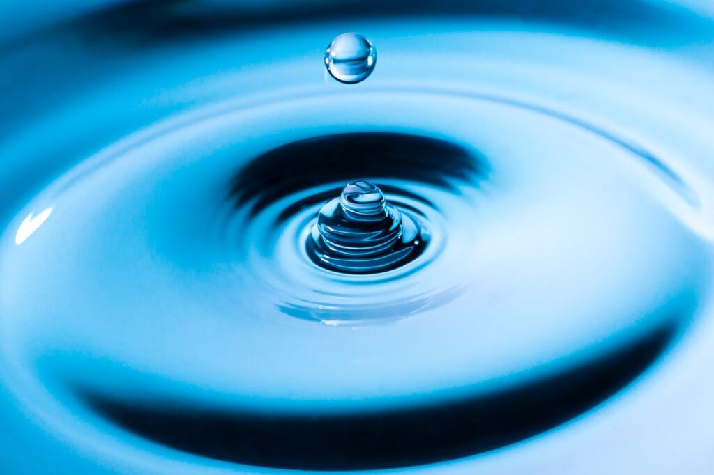 Close-up of a water droplet impacting a surface, creating ripples and splash in vibrant blue hues.