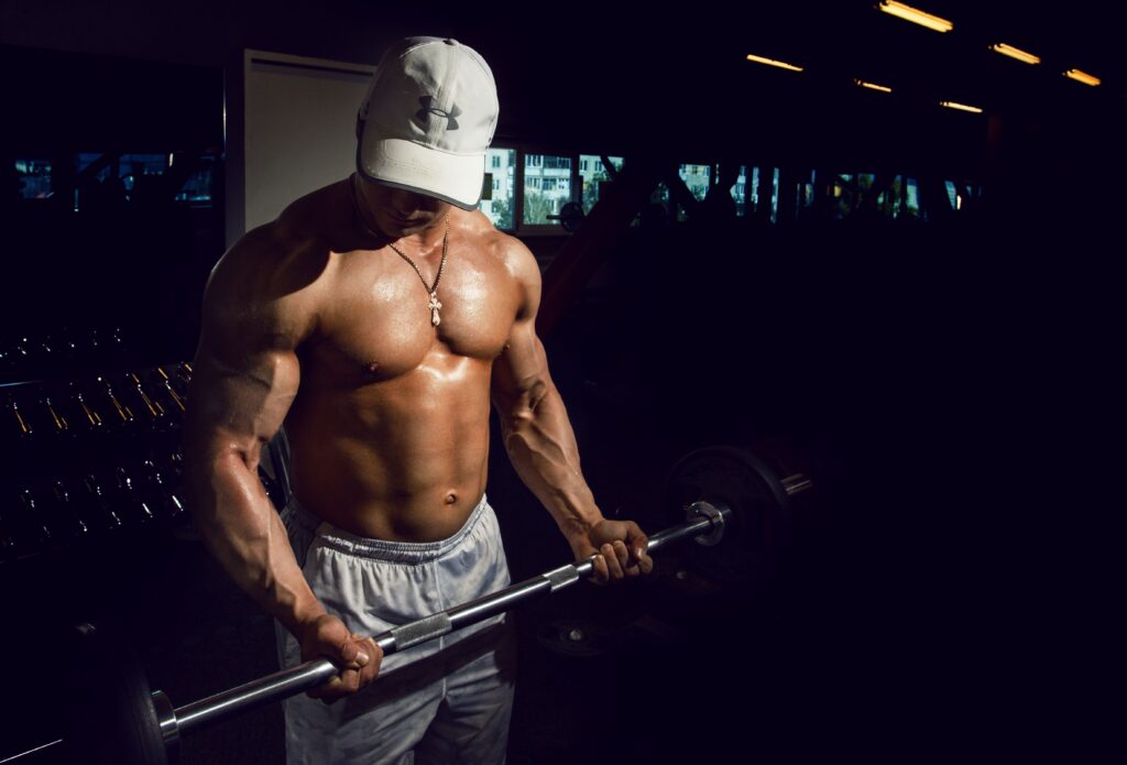 Strong shirtless man lifting barbell in a dimly lit gym, embodying fitness and strength.