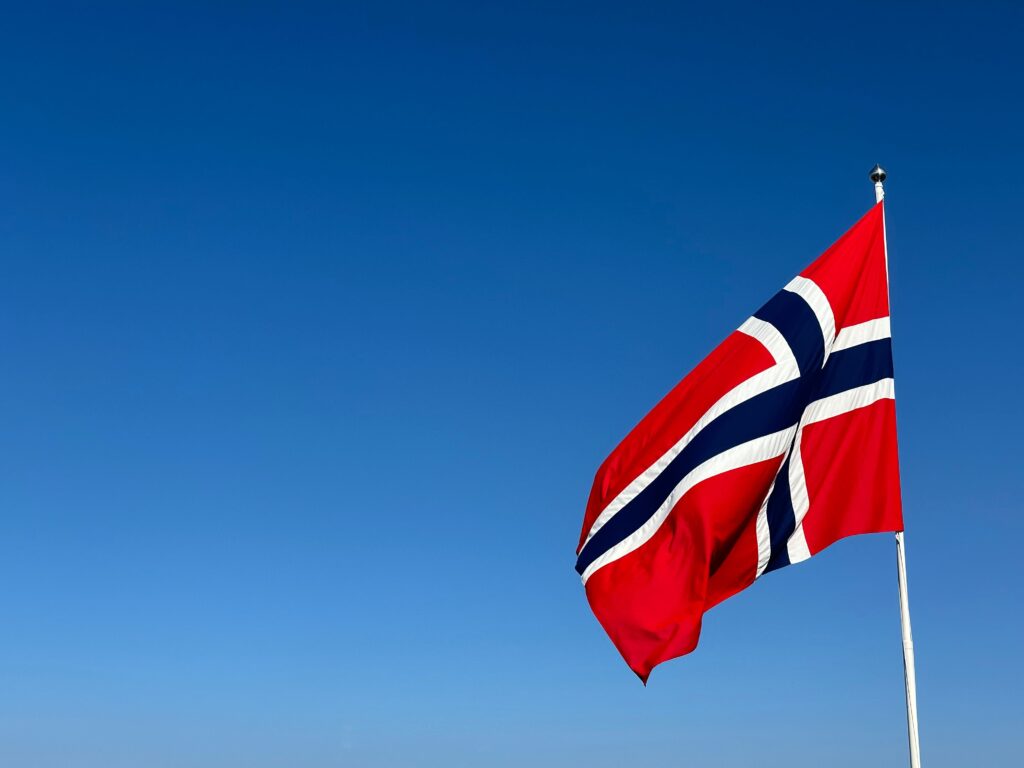 Norwegian flag waving in clear blue sky, symbolizing patriotism and national pride.