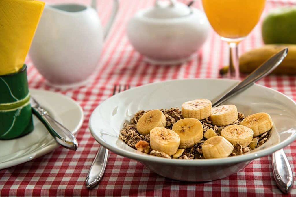 A healthy breakfast bowl with sliced bananas and cereal on a red checkered tablecloth.