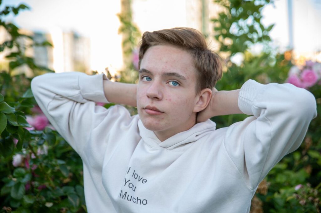 Teenager in white hoodie poses with hands behind head, surrounded by blooming roses.