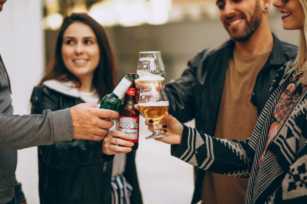Friends celebrating together and toasting with beer bottles and glasses outside.