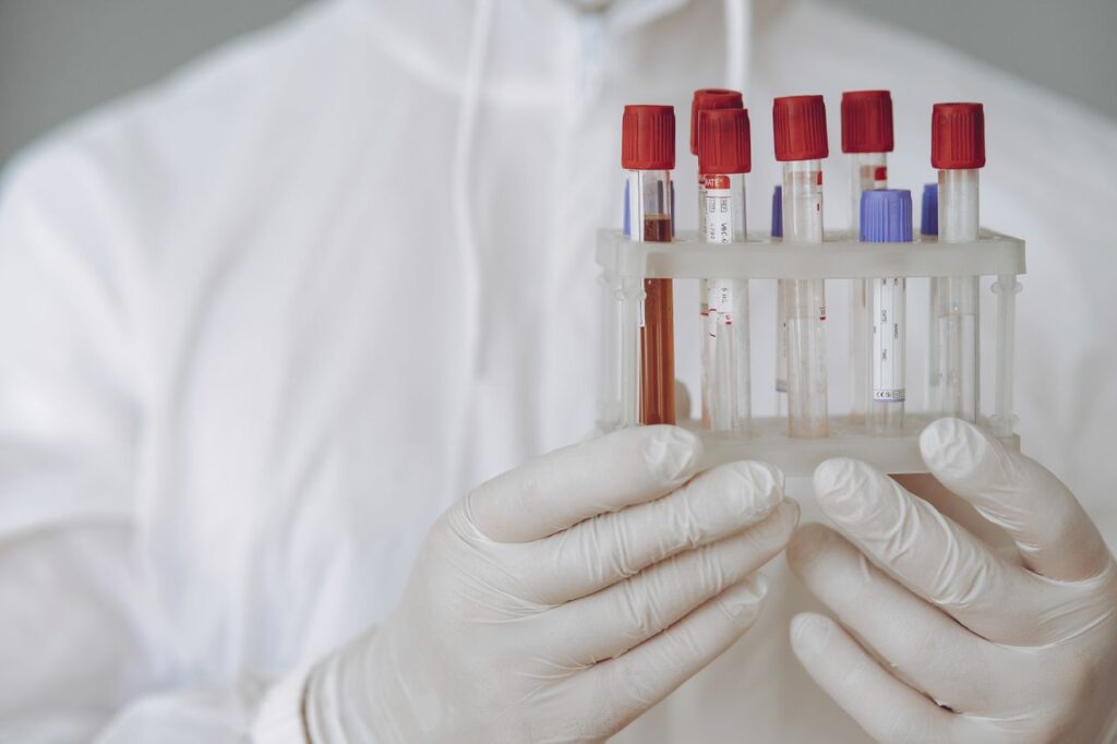Scientist in protective gear holding test tubes in a lab setting.