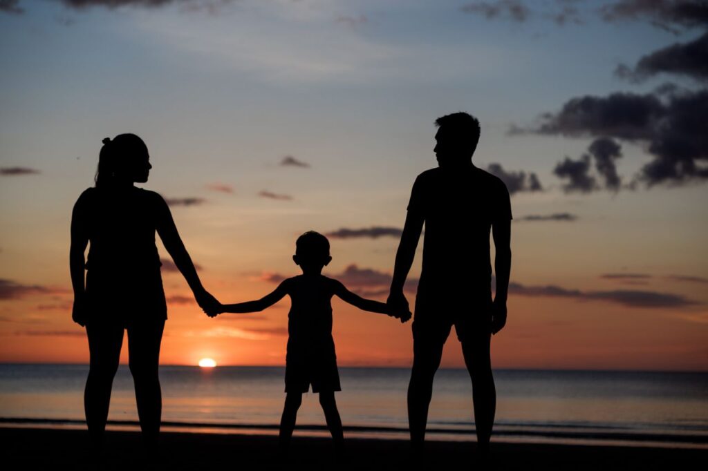 A silhouette of a family holding hands on a beach during a beautiful sunset.